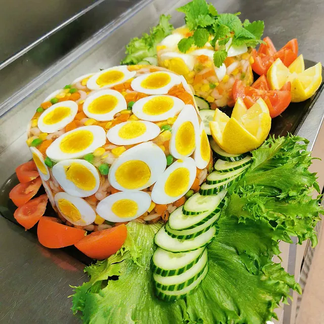 Kabaret dekorert med kokte egg, sitron, tomat og agurk, omgitt av frisk salat.