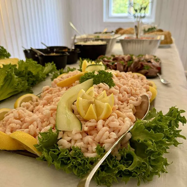 Serveringsbrett med reker, salat og sitron med flere retter i bakgrunnen.